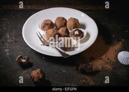 Placa blanca con trufas de chocolate caseras con mazapán y cacao en polvo sobre tabla oscura.