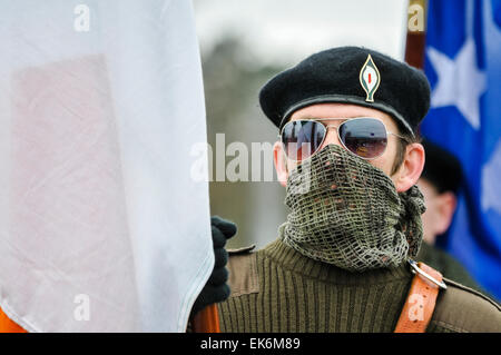 Un hombre enmascarado llevaba una lona sobre su boca, gafas de sol y una boina negra sostiene una bandera durante un republicano irlandés conmemoración Foto de stock