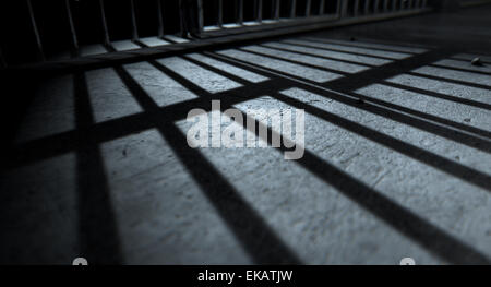 Un primer plano de vista de celdas barras de hierro que proyecten sombras en la cárcel piso con espacio de copia Foto de stock