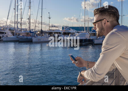 Joven utilizando el smartphone por puerto, Cagliari, Cerdeña, Italia