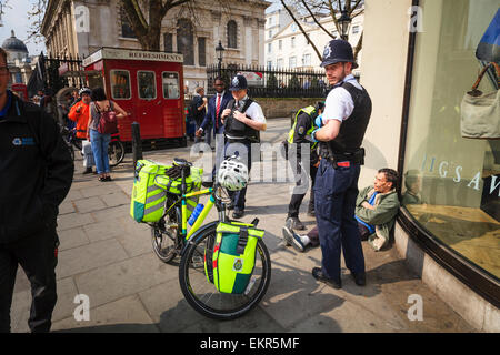 Dos policías de Londres Londres ayuda a un ciclo de ambulancia interviniente asistir a un hombre Foto de stock