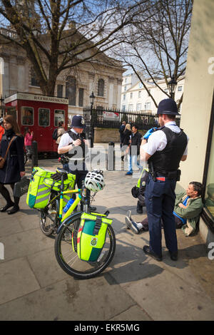 Dos policías de Londres Londres ayuda a un ciclo de ambulancia interviniente asistir a un hombre Foto de stock