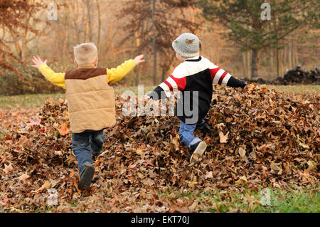 Dos muchachos saltar en la caída de la hoja montón