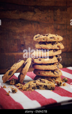 Pila de galletas con trocitos de chocolate en rojo y raya blanca servilleta contra un fondo de madera oscura.