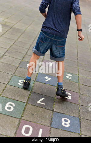 Niño jugando rayuela fuera en la acera Foto de stock