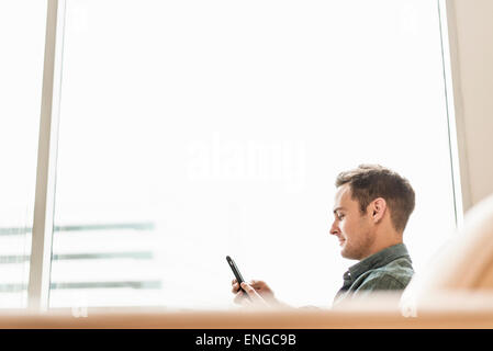 Un hombre sentado sosteniendo un teléfono inteligente comprobando sus mensajes. Foto de stock