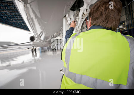 Mecánico en amarillo Hi Viz inspeccionando la nariz el tren de aterrizaje de un avión en una percha Foto de stock