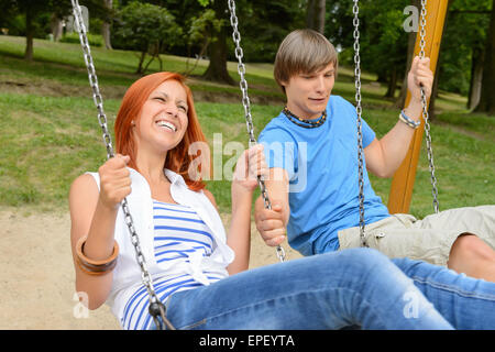 La pareja de adolescentes alegres en el columpio en el parque Foto de stock
