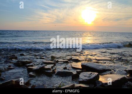 Reflexión costera al atardecer. El sol se pone en las orillas rocosas del Lago Michigan en la Península Superior. Foto de stock