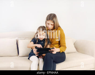 Niña con su madre utilizando dispositivo tableta en el sofá en casa, familia feliz, concepto tecnológico