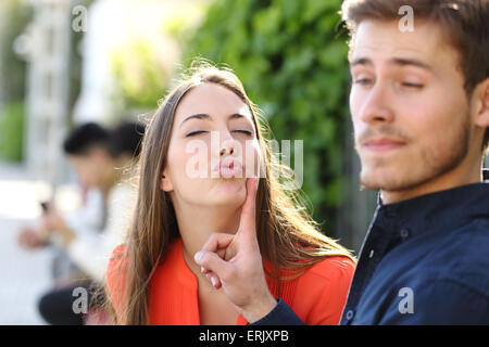 Mujer tratando de besar a un hombre y él está rechazando su piscina en un parque Foto de stock