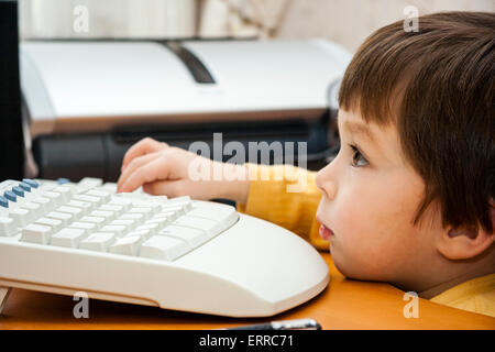 Vista lateral de primer plano de la cara de un niño caucásico, chico de 4-5 años, en el teclado de ordenador viendo pantalla invisible con expresión concentrada. Foto de stock