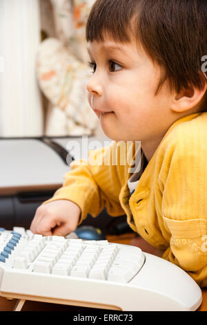 Vista lateral de primer plano de la cara de un niño caucásico, chico de 4-5 años, en el teclado de ordenador viendo pantalla invisible con expresión concentrada. Foto de stock