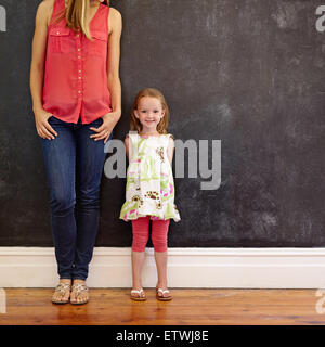 Filmación en interiores de hermosa niña de pie con su madre sonriendo. Madre e hija posando contra una pared negra con copia