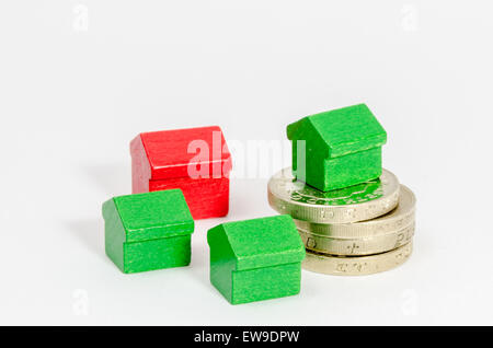 Pila de British Pound monedas con casas de madera roja y verde Foto de stock