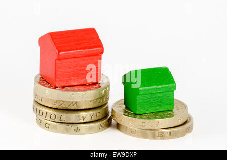 Dos pilas de British Pound monedas con casas de madera roja y verde. La mayor pila tiene la casa más grande Foto de stock