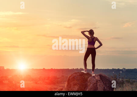 Joven mujer deportiva con los brazos levantados durante la puesta de sol en verano