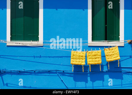 Tres almohadones amarillos colgando en la línea de fuera de la casa pintada de azul Burano Laguna de Venecia Veneto Italia Europa Foto de stock