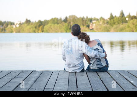 Vista trasera de una pareja sentada en un muelle de madera abrazando