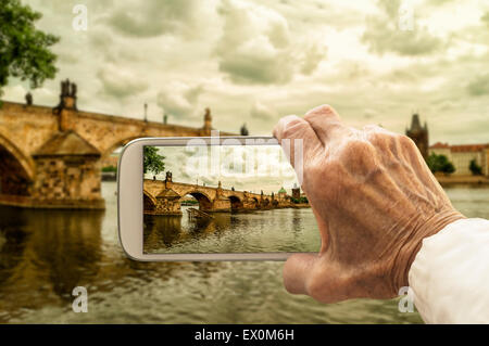Vieja mano toma una foto del Puente de Carlos en Praga, República Checa, el teléfono inteligente. El enfoque selectivo. Foto de stock