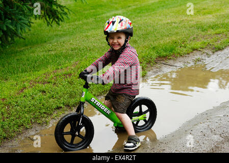 Un joven (3 años) montando bicicleta un equilibrio a través de un charco lodoso Foto de stock