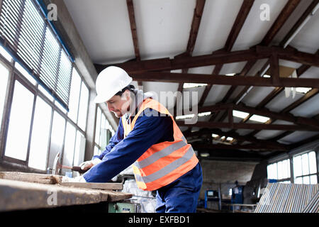 Trabajador de la fábrica martillando workbench en fábrica de refuerzo de hormigón