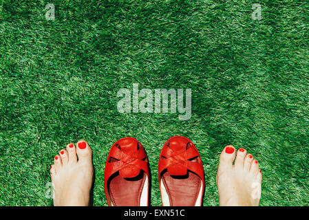Barefoot mujer con las uñas pintadas de rojo junto a un par de zapatos  rojos, sobre la hierba verde Fotografía de stock - Alamy