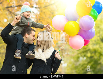Familia feliz con el niño pequeño y el aire globos, paseo en el parque de otoño Foto de stock