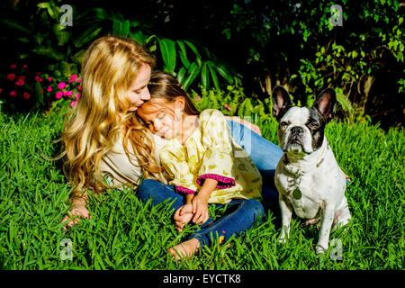 Mujer madura, la hija y el perro sentado en el césped del jardín