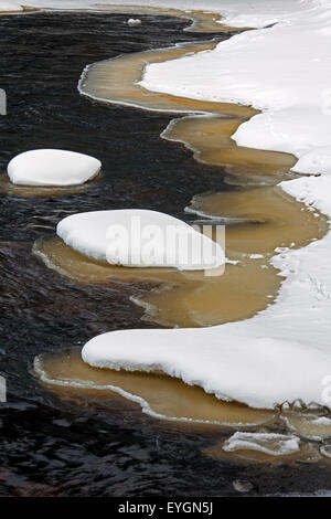 Brown hielo pastoso a lo largo de la ribera cubierta de nieve en invierno Foto de stock