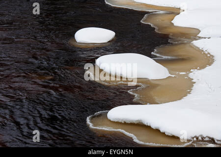 Brown hielo pastoso a lo largo de la ribera cubierta de nieve en invierno Foto de stock