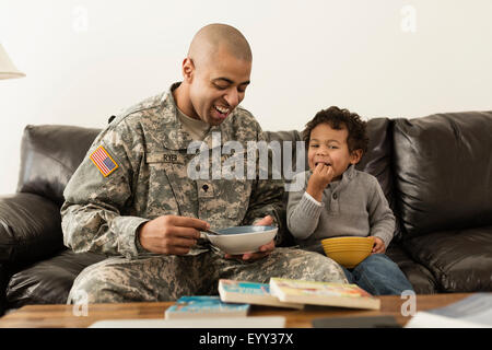Soldado de raza mixta, padre e hijo de bolos en el sofá Foto de stock