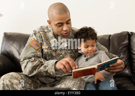 Soldado de raza mixta libro de lectura al hijo en el sofá Foto de stock