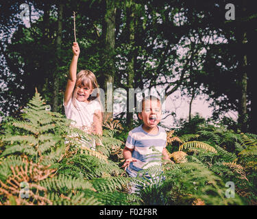 Dos niños felices saltando desde detrás de los helechos del bosque Foto de stock