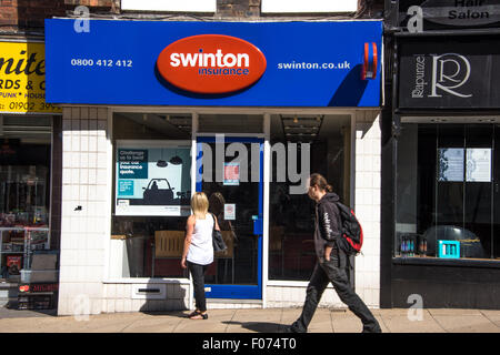 Una mujer mirando por la ventana de Swinton Insurance Services como un hombre camina pasado en High Street West Midlands en Wolverhampton, Reino Unido Foto de stock