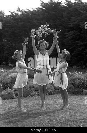 Dos chicas adolescentes con su madre bailando en un jardín luciendo vestidos con collares y pulseras de flores