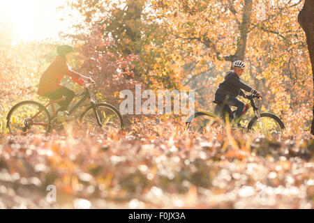 Chico y chica andando en bicicleta en hojas de otoño