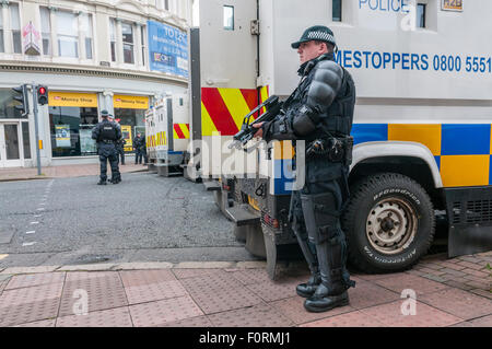 PSNI armada policía posee una Heckler & Koch G36C ametralladora automática en una calle de Belfast como vehículos blindados bloquean carretera Foto de stock