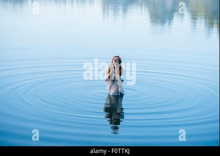 Mujer joven de pie en el lago ripples orando con los ojos cerrados