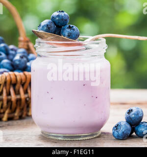 Arándanos frescos yogurt de jarra de cristal y cesta de mimbre con arándanos azules sobre fondo. Foto de stock