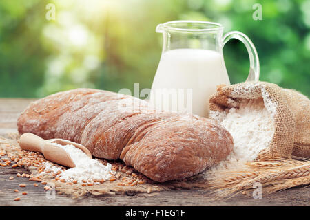 El pan, una jarra de leche fresca, el saco de harina y trigo oídos sobre mesa de madera. Foto de stock