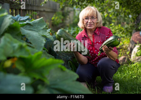 Mujer con un gran calabacín sosteniendo en las manos en el jardín de su casa. Foto de stock