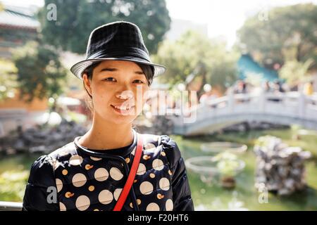 Retrato de joven mujer vistiendo sombrero en frente de los jardines chinos puente, mirando a la cámara