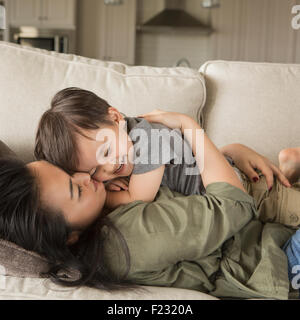 Una mujer recostada en un sofá, sonriente, abrazando a su pequeño hijo.