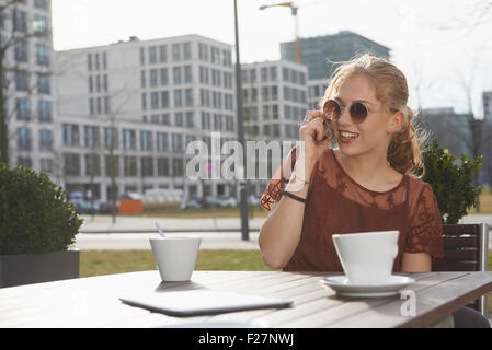 Mujer joven hablando por un teléfono móvil en el café en la acera, Munich, Baviera, Alemania Foto de stock