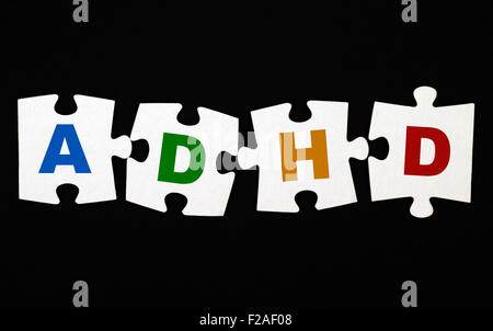 Cuatro piezas de rompecabezas con letras TDAH sobre fondo negro. El TDAH es el trastorno por déficit de atención con hiperactividad. Foto de stock