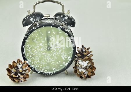 Cierre de un reloj despertador retro negro nevados, mostrando el tiempo de invierno, 2 am, con conos de pinos sobre fondo blanco, horizontal
