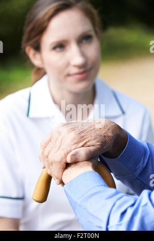Las manos del hombre Senior Descansando sobre un bastón con cuidado Trabajador en segundo plano.
