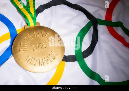Río de Janeiro, Brasil - Febrero 3, 2015: Gran medalla de oro conmemorativa de los Juegos Olímpicos del 2016 se asienta sobre la bandera olímpica antecedentes Foto de stock