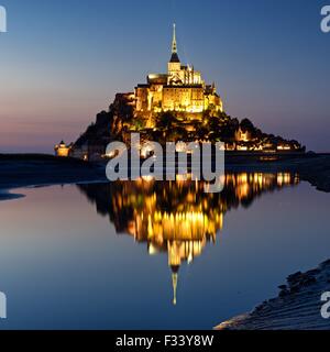 Una imagen a color de las reflexiones de Mont Saint Michel iluminado al anochecer, en una piscina de agua en la playa de Mont Saint Michel. Foto de stock